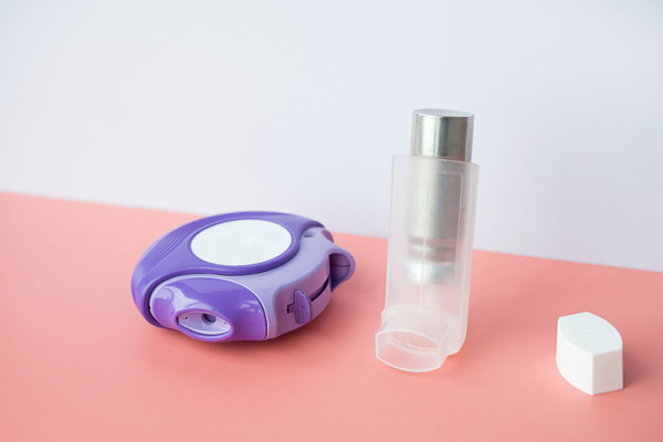 An angled pink counter holding two types of asthma inhalers, one a purple disk, the other silver and frosted plastic and has a white top next to it